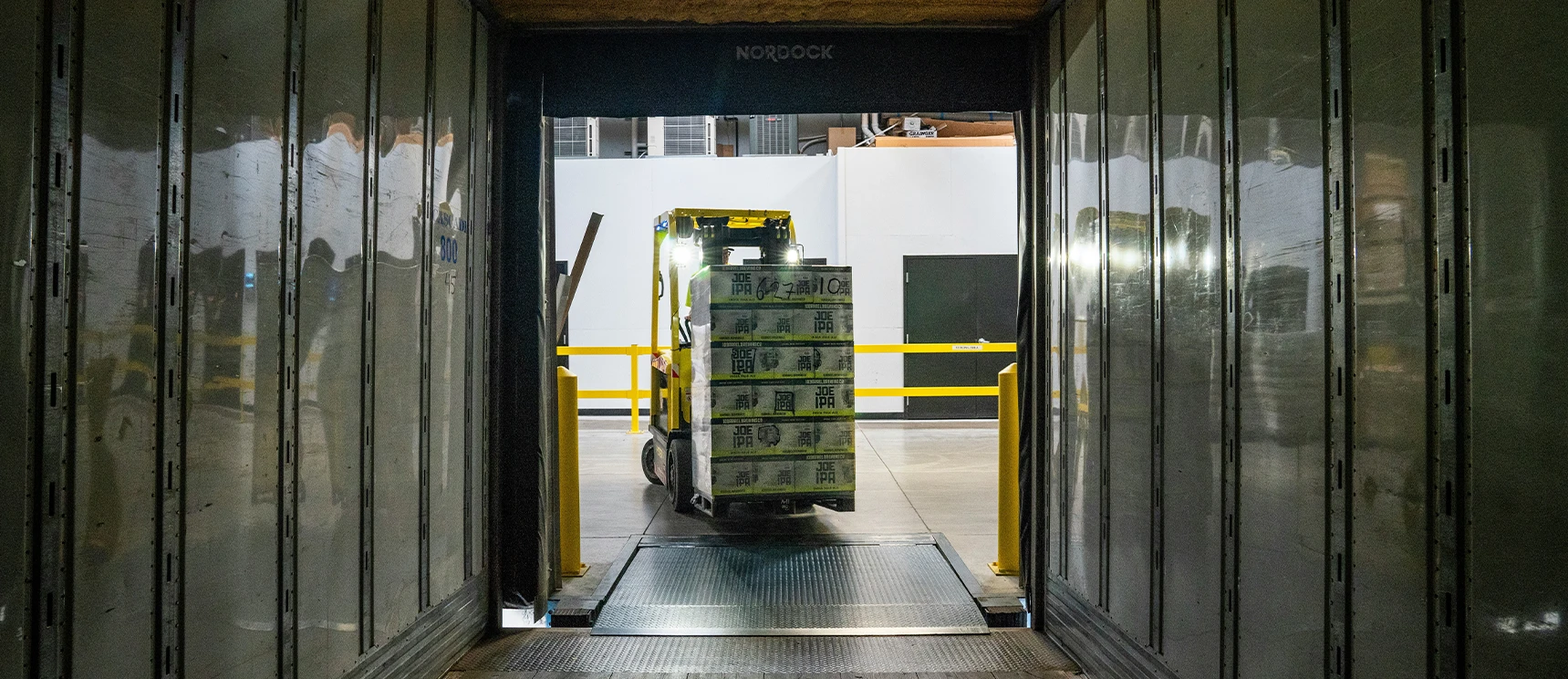 A forklift transporting boxed goods enters a loading dock area in a warehouse.