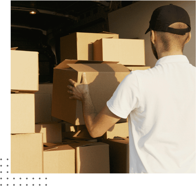 A man wearing a white shirt and black cap is loading several cardboard boxes into a vehicle.